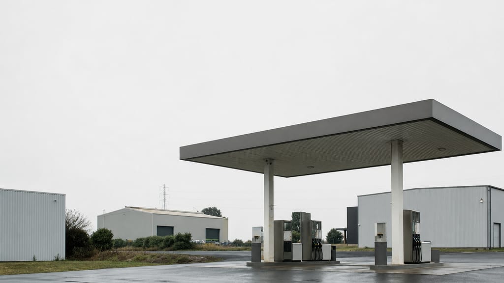 Illustration Station-service en zone d’activité périurbaine française, entrepôts flous derrière — ambiance station-service type Station indépendante — Voie Romaine à Quissac, en ville (photo éditoriale, non contractuelle)